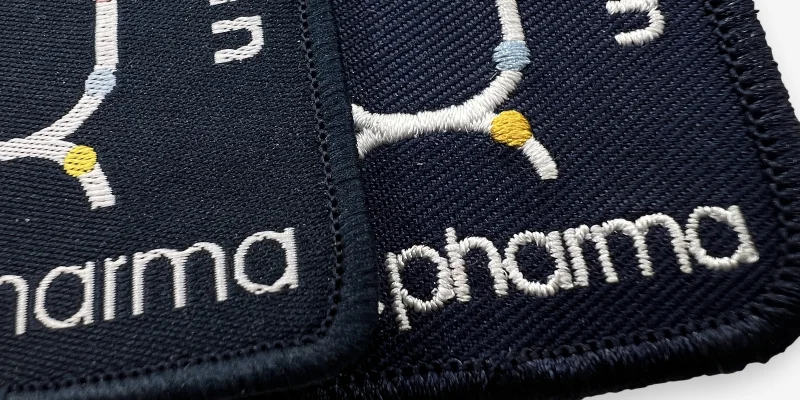 Ett vävt tygmärke bredvid ett brodyrmärke för jämförelse.