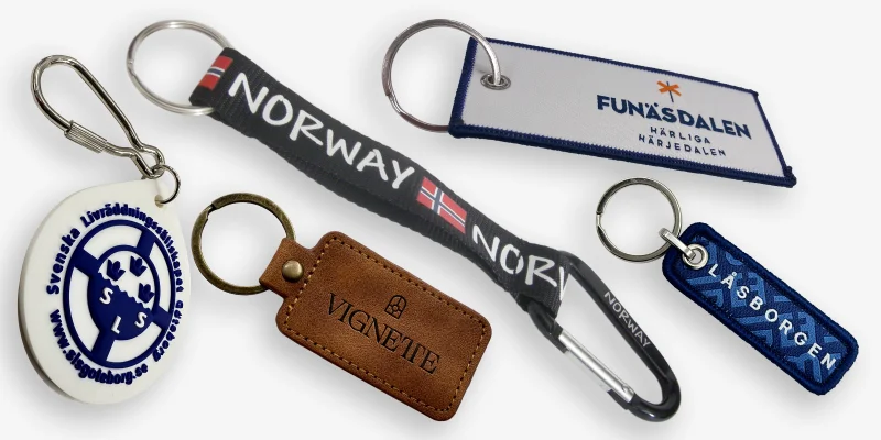 Två tygnyckelringar av broderad och vävd typ med olika färger och loggor samt en gummi- och lädernyckelring och en short-strap.