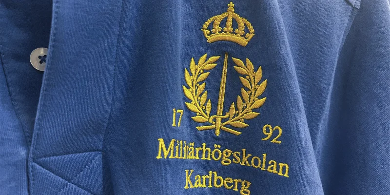 Blå pikétröja med broderad logotyp i gul färg.