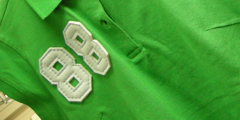 Grön figursydd ärmlös piké med vit logga tillverkad med applikationsbrodyr.