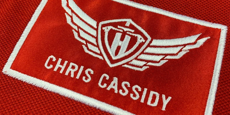 Aplikationsbrodyr på piké med namn och logotyp.